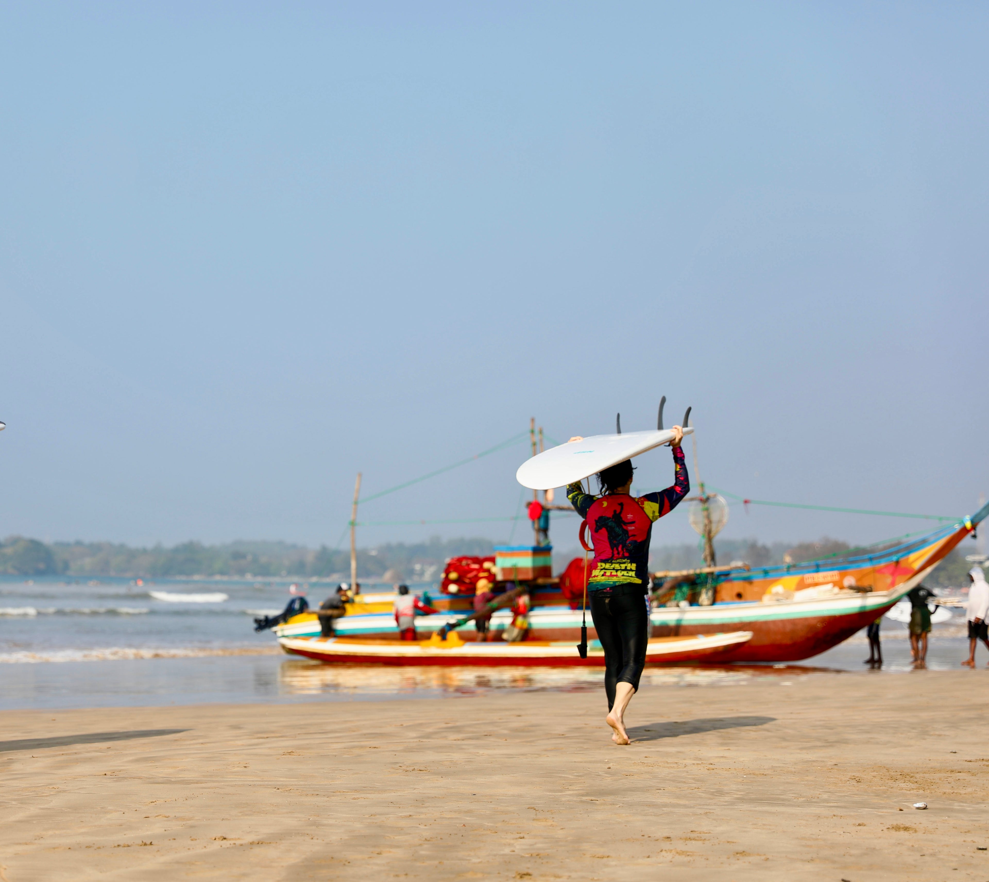 Person walking on a beach with colorful boats in the background