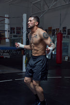 Man in a gym wearing boxing gloves and shorts, preparing to box.