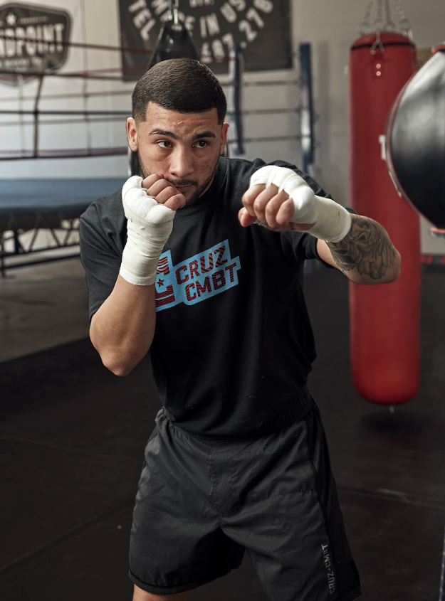 Boxer in a gym wearing a black 'Cruz Combat' shirt and white boxing gloves.