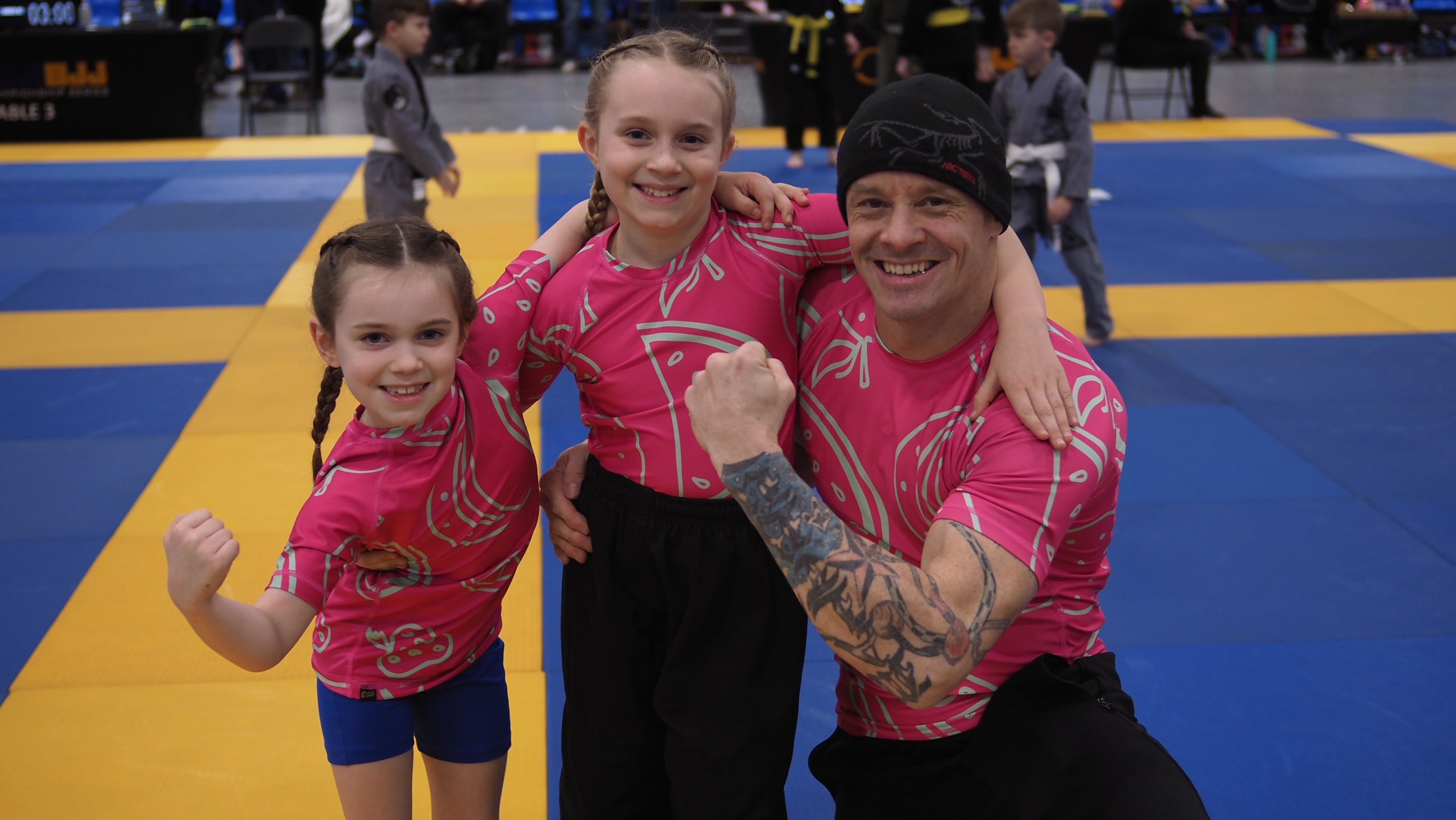 Family of three in pink outfits on a blue and yellow mat
