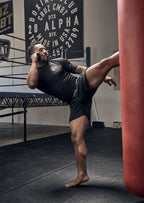 Person practicing martial arts in a gym setting with punching bags and boxing club posters.